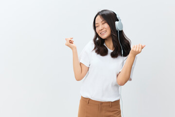 Obraz na płótnie Canvas Enjoying happy joyful cute Asian young female in white basic t-shirt moves to cool songs playlist posing isolated on over white studio background. The best offer for ad. Favorite Music App Ad concept