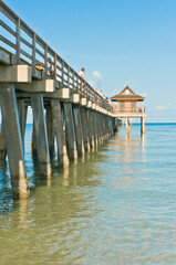 front view, medium distance of a tropical pier jutting out from a sandy beach with people watching porpoises feeding on a sunny morning