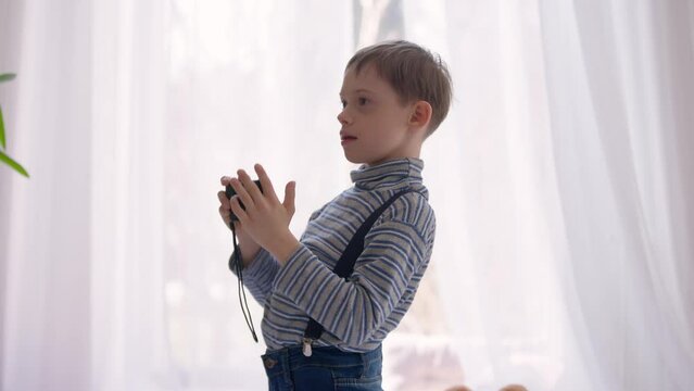 Side view hyperactive autistic boy taking photos with camera indoors. Talented Caucasian child with mental disorder enjoying hobby standing at home. Autism and activity concept