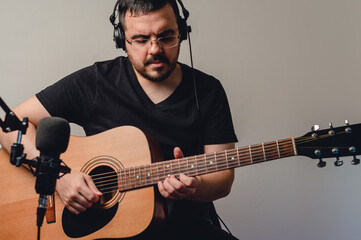 portrait young caucasian man recording acoustic guitar in home studio, front view