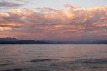 Obraz premium Long exposure shot of Nahuel Huapi lake and the Andes mountains in the background, at sunset. Beautiful blurred water effect, the rocky shore and dusk colors in the sky.