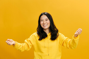 Yeah, I did it. Overjoyed Asian student young woman in yellow hoodie sweatshirt raise fists up smiling posing isolated on over orange studio background. Cool offer. People Emotions concept