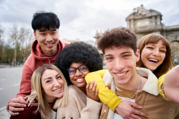 Smiling selfie of a group of happy friends outdoors in the city. Young tourists take pictures of their vacation with a smart phone. People having fun on a student trip in Europe.