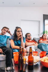 sad friends watching TV because their football team lost the game. upset young people at a house...