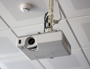 White overhead multimedia projector hanging on the ceiling in university
