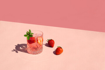 Minimal concept a glass of cocktail with strawberries and ice cubes on pink background. Summer...