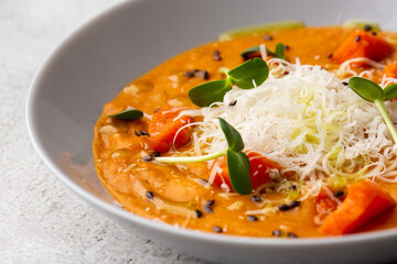 Pumpkin traditional soup with creamy silky texture, garnished with tomatoes and parmigiano. Marble background. Copy space. Top view