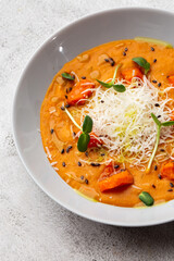 Pumpkin traditional soup with creamy silky texture, garnished with tomatoes and parmigiano. Marble background. Copy space. Top view