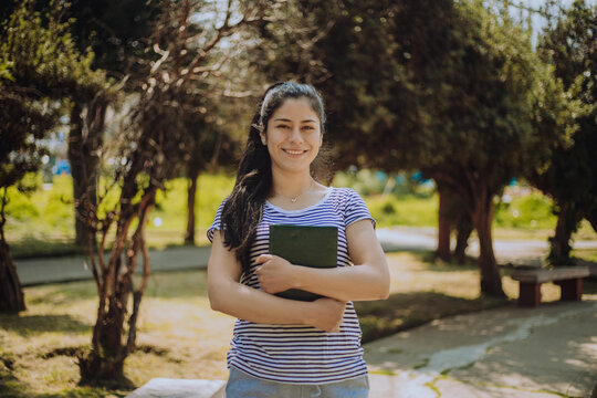 Retrato de joven estudiante sosteniendo un libro al aire libre. Concepto de educaci&oacute;n.