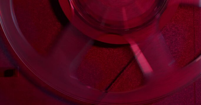 Old reel-to-reel tape recorder plays magnetic tape record closeup. Turntable in dark red light. 