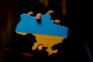 a map of Ukraine carved from wood and painted in the colors of the Ukrainian flag in the hands of a girl on a dark background