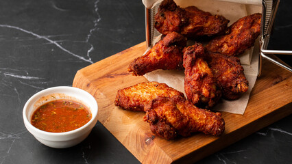 Fried Chicken Wings Covered in True Hot BBQ Sauce served with red hot chilli sauce on a Cutting Board on marble background.
