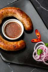 Juicy homemade baked sausage on a plate with spicy sauce and marinated onion on marble background.