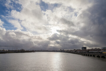 Fototapeta premium Winter Panorama of the estuary of the garonne river seen from Garonne quay (Quais de la Garonne) in bordeaux, France, with the old buildings of the city center in background and a cloudy gray sky.....
