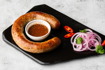 Juicy homemade baked sausage on a plate with spicy sauce and marinated onion on marble background.