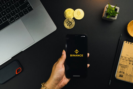 Girl holding a smartphone with Binance cryptocurrency exchange app on the screen on black table with a cryptocurrencies coins and computer. Office environment. Rio de Janeiro, RJ, Brazil. April 2022