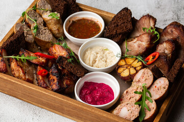Close-up photo of mixed grilled meat platter. Beef, pork, poultry, sausages, grilled garlic, chili pepper, different sauces on marble background.