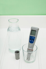 pH meter in a glass of water, and bottle on a white and green background. Measurement of the...