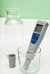 pH meter in a glass of water, and bottle on a white and green background. Measurement of the...