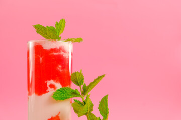 Summer drinks. Strawberry cocktail.Berry smoothies. Pink cocktail and cream in a transparent glass goblet with strawberries and sprigs of mint on a pink background.