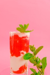 Summer drink. Strawberry cocktail.Berry smoothies. Pink cocktail and cream in a glass goblet with strawberries and sprigs of mint on a pink background.Drink from summer berries