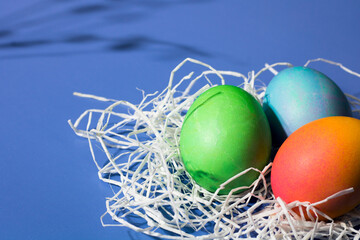 Three beautiful Easter eggs lie in a decorative white nest close-up.