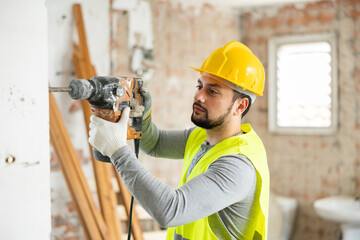 Portrait of positive man builder posing with handheld demolition hammer at indoor construction site