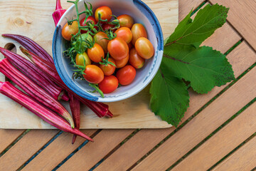 Home grown Grappoli d’Inverno tomatoes in a blue and white bowl and Jing orange okra on a cutting board, flat lay view from above. 