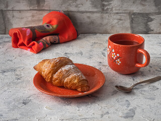 Breakfast with croissant and tea in an orange mug with a pattern