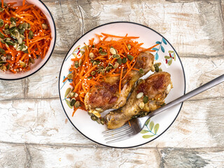 Fried chicken drumsticks carrot salad with seeds on a colored plate