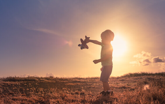 Little child playing with airplane at sunset. Happy childhood concept. 