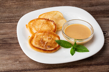 Pile of freshly fried thick pancakes, in Eastern European cuisines called oladky or oladyi with condensed milk on wooden background