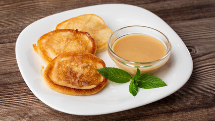 Pile of freshly fried thick pancakes, in Eastern European cuisines called oladky or oladyi with condensed milk on wooden background