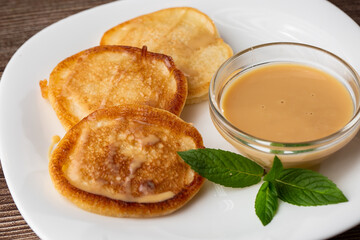 Pile of freshly fried thick pancakes, in Eastern European cuisines called oladky or oladyi with condensed milk on wooden background