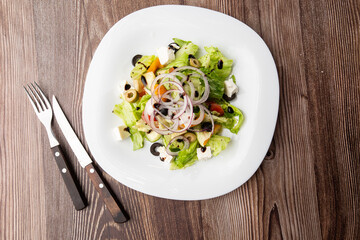 Greek salad with fresh vegetables: tomato, cucumber, red bel pepper, lettuce, onion, olives and cheese. Close-up on a wooden background.