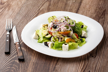 Greek salad with fresh vegetables: tomato, cucumber, red bel pepper, lettuce, onion, olives and cheese. Close-up on a wooden background.