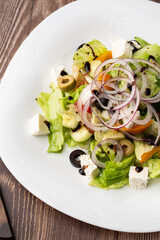 Greek salad with fresh vegetables: tomato, cucumber, red bel pepper, lettuce, onion, olives and cheese. Close-up on a wooden background.