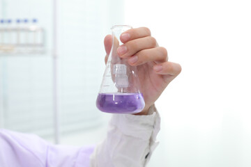 Close-up of a scientist's hand holding a lab flask containing chemical solutions. Shake the bottle with the chemicals.