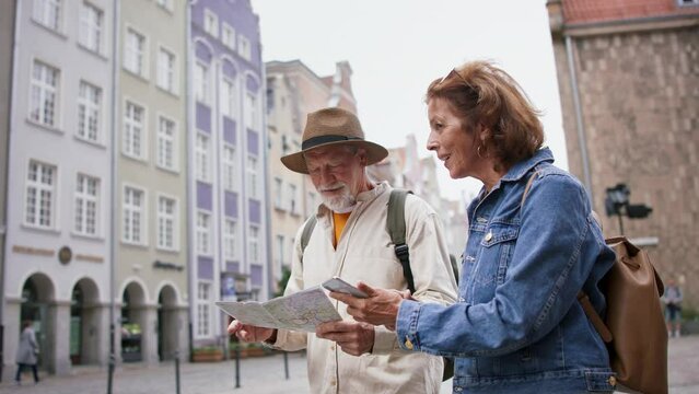 Happy senior couple tourists using smartphone and map outdoors in historic town