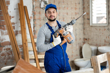Portrait of a professional builder standing on a construction site indoors, holding a hammer drill in his hands
