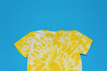 Beautiful white and yellow tie dye T-shirt on a blue background. Flat lay.