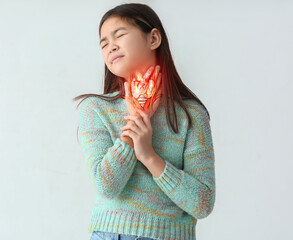 Ill Asian girl with pain in throat on light background