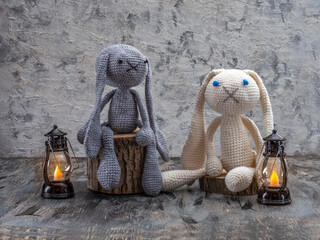 Handmade toys, amigurumi, crocheted bunnies sitting on stumps and lit lanterns
