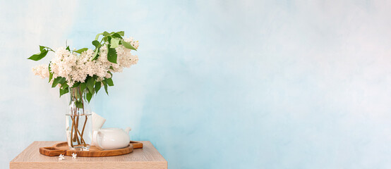 Vase with bouquet of beautiful white lilac and teapot on table against light blue background with space for text