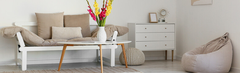 Interior of light living room with sofa, table, beanbag and chest of drawers. Banner for design