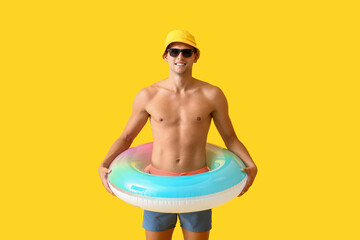 Attractive young man with inflatable ring on yellow background