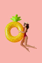 Jumping young woman with inflatable ring on pink background