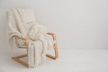Armchair with white blanket and cushion near light wall