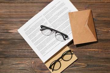 Stylish eyeglasses with book and envelope on wooden background