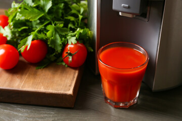 New modern juicer and glass of fresh juice with tomatoes on table, closeup